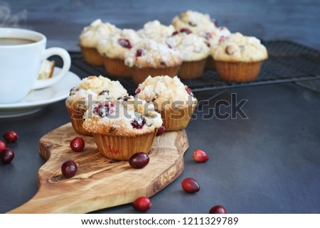 Cranberry Muffins on a wood cutting board with more cooling on a bakers rack. Extreme shallow depth of field with selective focus on muffin in foreground. Steaming hot cup of coffee in the background.