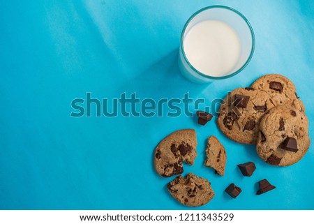 Flat lay picture of chocolate cookies and a cup of milk on blue color background