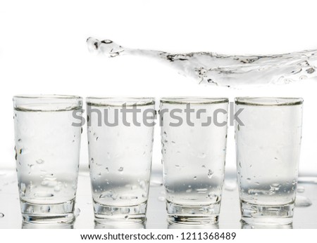 Four shot glasses close up with a splash of water in them and flying water over them