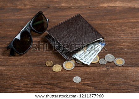 
leather wallet with dollars and sunglasses on a wooden background with pennies