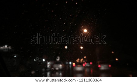 Blurred image, Rain falling on car windshield, Colorful bokeh with street light at night. Traffic in the city on rainy day, blur and dark background.