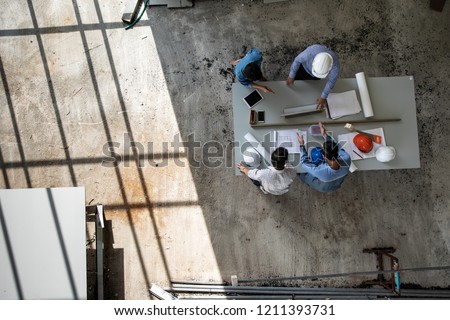 Four persons professional team of engineers talk together to review material in construction site, taken from high angle, top view photo with shadow of window frame on floor.