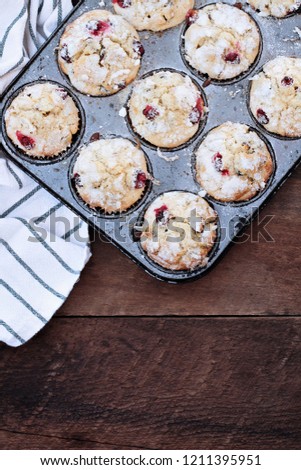 Cranberry Muffins  in a muffin tin with kitchen towel over a rustic wood  background. Free space for text.