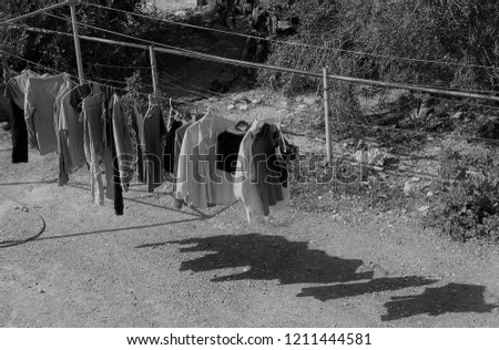 monochrome picture of clothes hanging on outdoor line. Sharp shadows of the washing on ground.