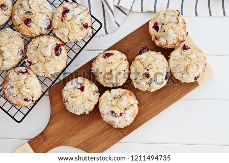 Fresh cranberry muffins cooling on a bakers rack and a wood cutting board over a rustic white table  background. Image shot from above with free space for text.