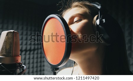 Beautiful girl singing in sound studio. Young singer emotionally recording new song. Lady sings to microphone. Working of creative musician. Show business concept. Slow motion Close up.