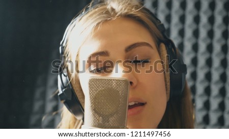 Portrait of beautiful girl singing in sound studio. Young singer emotionally recording new song. Lady sings to microphone. Working of creative musician. Show business concept. Slow motion Close up.