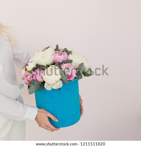 Woman with flowers in a hat box. Bouquet of peonies. Women's hands holding a gift box with flowers, Blue box. free space for text