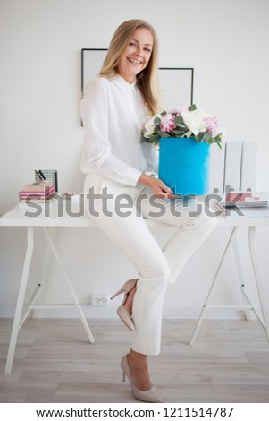 Stylish young blonde in office, white shirt and pants. Holds a luxurious bouquet of peonies in a blue hat box. free space for text