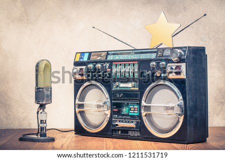 
Retro old ghetto blaster stereo radio cassette tape recorder boombox from circa 1980s, large studio microphone and golden star front concrete wall background. Vintage instagram style filtered photo