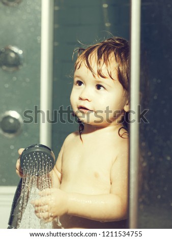 Cute happy smiling funny undressed boy child with blonde curly wet hair taking shower in bath with water indoor, vertical picture