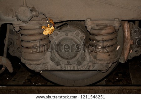 A fragile yellow leaf that stuck in the hard steel coil spring of a rail car bogey