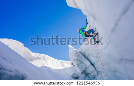 Epic shot of an ice climber climbing on a wall of ice. Mountaineer, climber or alpinist on an adventure extreme ascent with ice axe and crampons. Alpine extreme climbing on a serac or creavasse. Royalty-Free Stock Photo #1211546956