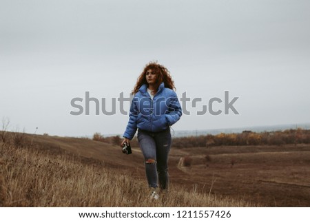 A beautiful girl with red hair travels in spacious fields and meadows, drinks thermos tea and admires the scenery.
