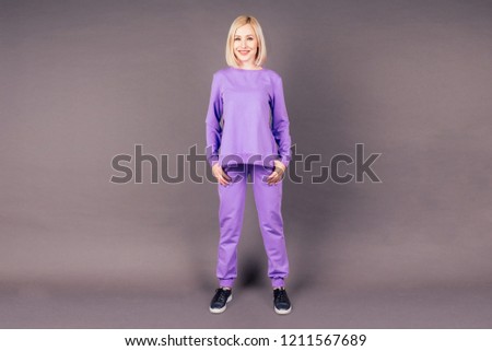 full-length portrait of a beautiful makeup blonde woman slim in violet sports suit posing and stretching in the studio on a black background,hip hop dancer dancing happy model smiling