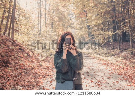 Brunette girl taking pictures of autumn forest on phone