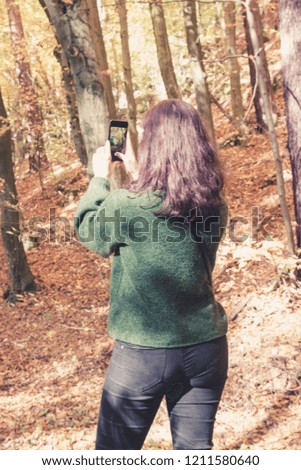 Brunette girl taking pictures of autumn forest on phone