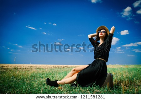photo of the beautiful young woman sitting on the suitcase in the field