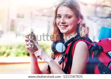 Tourist girl with backpack and headphones taking selfies on smartphone at cultural city pedestrianized street outdoor. Sending photos from smartphone.