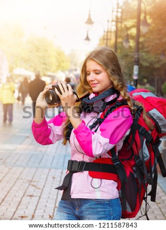 Tourist girl with backpack and headphones taking pictures on dslr camera at sunset autumn cultural city pedestrianized street outdoor.