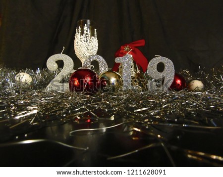 Happy New Year 2019 background. Silver, shiny candles numbers with christmas decoration on black background, and white decorative champagne glass