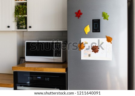 Colorful felt autumn leaves on refrigerator door. White kitchen on background. Diy fall autumn decoration for home