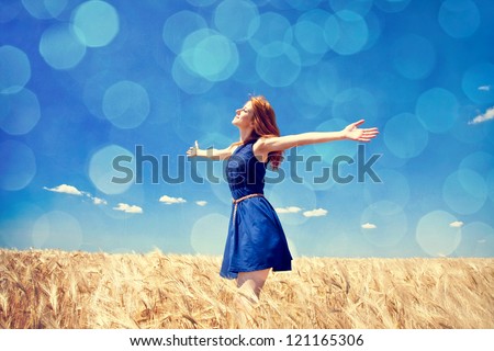 Redhead girl at wheat field in summer day. Photo with bokeh at background.