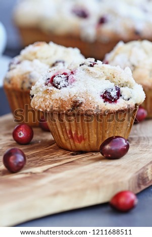 Cranberry Muffins with lemon sugar topping on a rustic cutting board with loose berries. Extreme shallow depth of field with selective focus on muffin in foreground.