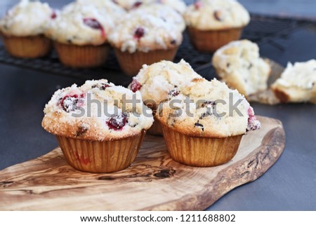 Cranberry Muffins with lemon sugar topping on a rustic cutting board with loose berries. Extreme shallow depth of field with selective focus on muffin in foreground.