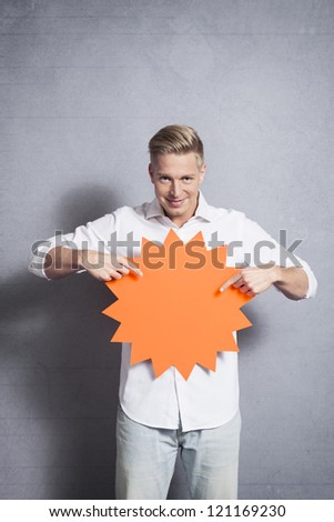 Confident handsome man pointing fingers at blank panel with space for text promoting sales isolated on grey background.