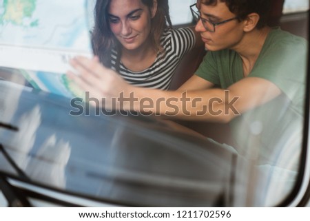 portrait of young couple inside car using a map on a road trip for directions