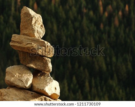 Person shaped rock sculpture facing out towards a heavily forested mountain