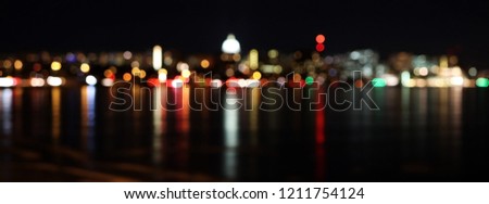 Abstract bokeh night city lights background. Silhouette of Madison skyline at night with out of focus street lights and glowing in the dark state Capitol building reflected in a lake water at night. 