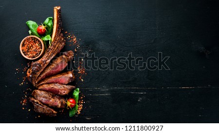 Steak on the bone. tomahawk steak On a black wooden background. Top view. Free copy space. Royalty-Free Stock Photo #1211800927