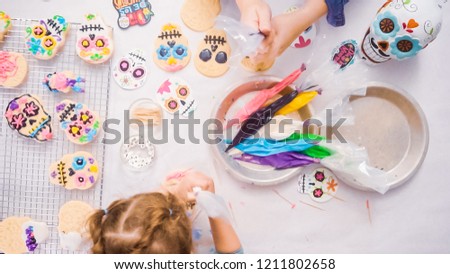 Step by step. Flat lay. Mother and daughter decorating sugar skull cookies with royal icing for Dia de los Muertos holiday.