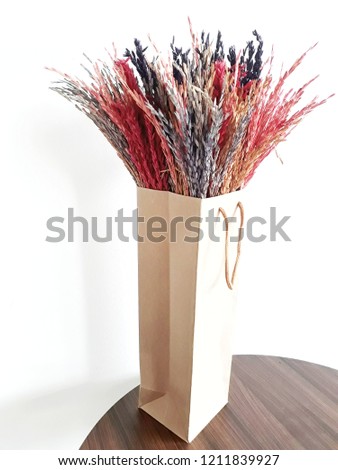 Dried flowers in a tall paper bag with white walls as a backdrop.