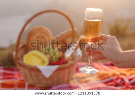 Cheers! Cropped image Hand with glass of champagne at sunset over picnic basket with food.