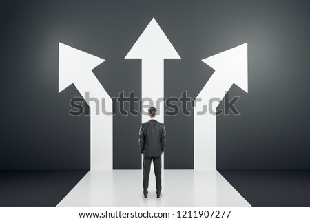 Back view of young businessman standing on black background with three arrows. Different direction and success concept