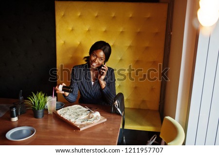 African american businesswoman eating cheese pizza in cafe. Black girl having rest and speaking on phone.