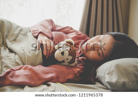 Closed up image of an Asian woman sleeping and hugging a cute doll in bed with gray blanket , flare lighting from the window.