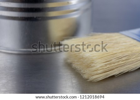 A paint brush and a can of paint on a workshop table. Painting accessories for construction workers. Light background.