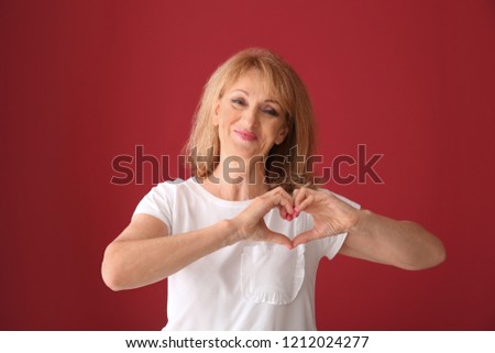 Portrait of mature woman making heart with her hands on color background