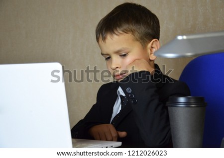 Young businessman using a laptop. funny child. Fashion portrait of little handsome boy in office sits by the table