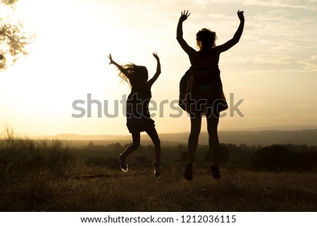 Backlight of a mother and her daughter walking holding hands in a pine forest with yellow sky