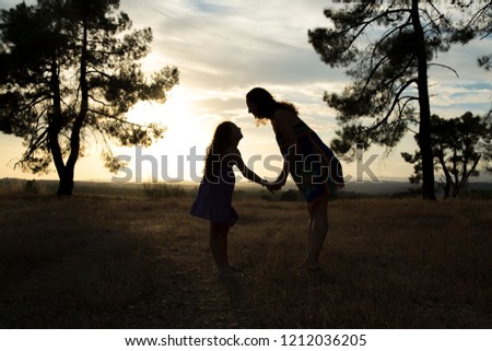 Backlight of a mother and daughter in a pine forest with yellow sky