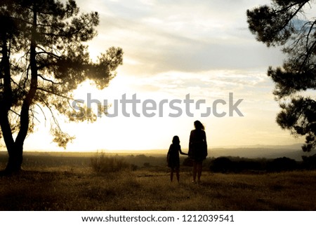 Backlight of a mother and daughter in a pine forest with yellow sky