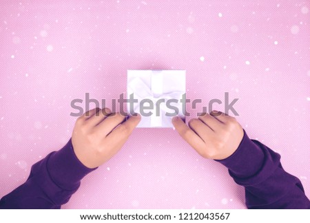 Top view of hands holding a small box with a gift and a ribbon on a blue background.