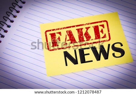 Sheet of yellow post note paper or self-adhesive notes written Fake News with background notebook.