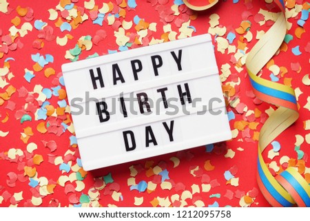 happy birthday greeting - flat lay design with confetti and streamer - text on lightbox sign on red background