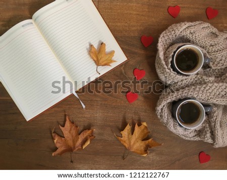 Two cups of coffee, cozy warm scarf, open book,leaves and heart decoration on wooden table. Top view.